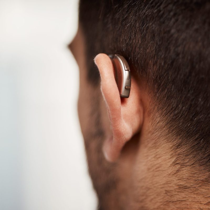 Closeup of hearing aid, ear and man with disability from the back for medical support, listening or.